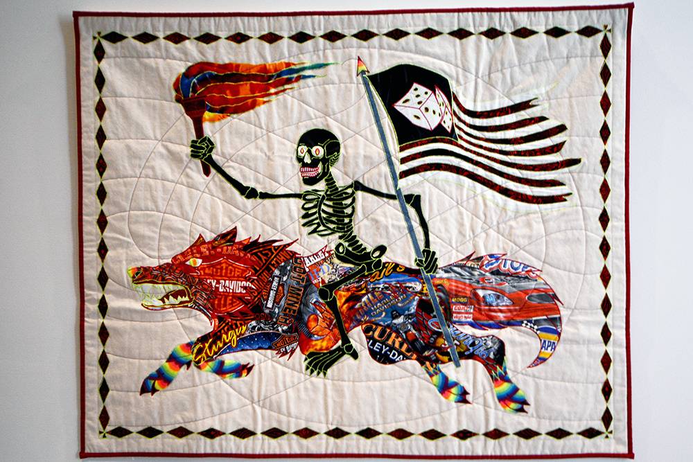Patchwork quilt depicting a skeleton riding a wolf, holding a flag and torch.